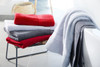 A stack of bath towels in red, grey, and white, arranged neatly on a metal stand beside a bathtub.