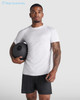 A man wearing a white Montecarlo T-shirt and black shorts holds a fitness ball, posing against a light background.