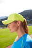 A bright yellow 6 panel sport mesh cap is worn by a woman with a ponytail, set against a grassy field backdrop.