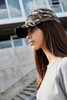 A camouflage 6-panel cap featuring a curved brim, worn by a model with long hair. It has a logo on the front.