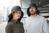 A black and navy cap with a wide neck guard, worn by a man and woman in casual clothing.