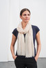 A light beige scarf draped around a woman's neck, wearing a navy top and standing against a plain background.