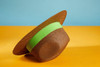 A brown Traveller Hat with a green band, featuring a wide brim, displayed against a blue and orange background.