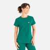 A green scrub top with a round neck, featuring a pocket and a small logo on the chest.