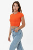 An orange cap sleeve crop top is displayed, paired with light blue jeans. The shirt features a simple design and has a logo.