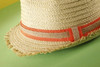 A straw hat with a frayed edge and a coral band, set against a green background.