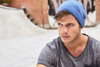 A blue beanie worn by a man, set against an urban background with a textured surface.
