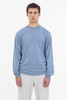 A long sleeve crewneck tee in a soft blue colour, worn by a model with grey pants. It features a small logo.