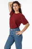 A woman poses in a maroon short sleeve cotton poly crew tee, paired with high-waisted blue jeans. The tee has a logo.