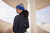 A reversible beanie in grey and blue, worn by a person with curly hair, standing outdoors near architectural features.
