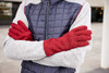A pair of red fleece gloves worn by a person with crossed arms, dressed in a grey and navy jacket.