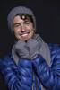 A man in a grey beanie and scarf, smiling, wearing a blue puffer jacket. The image features a logo on the scarf.