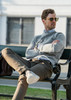 A grey sweatshirt worn by a man sitting on a bench, paired with beige trousers and sunglasses.
