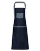 A denim bib apron in dark blue with contrasting light blue straps and pockets. It has a logo displayed.
