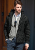 A man wearing a black soft shell jacket over a grey sweater, styled with sunglasses and smart trousers.