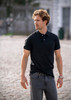 A black polo shirt worn by a man with wavy hair, paired with grey jeans, standing outdoors. The shirt features a logo.