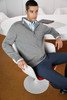 A grey zip cardigan worn by a man seated in a chair, accompanied by a blue shirt and navy trousers.