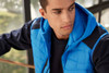 A men's hybrid vest in bright blue with a hood, featuring a quilted design and a navy base layer.