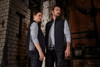 A padded hybrid vest in black, worn by a man and a woman, featuring a logo, set against an industrial backdrop.