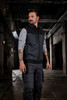 A man wearing a black and grey hybrid workwear vest in an industrial setting, showcasing a sleek design.