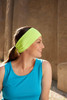 A running headband in bright yellow-green worn by a woman with long hair, paired with a blue tank top.