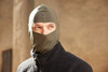 A balaclava in olive green, worn by a person, with a zippered black jacket in the background.