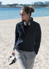 A women’s navy jacket with a high collar, paired with grey pants, worn by a model on a sandy beach.