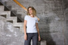 A white ladies T-shirt with a fitted design, displayed against a textured concrete wall and staircase.