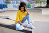 A yellow oversized T-shirt paired with light blue jeans, worn by a person sitting at a skate park.