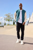 A varsity jacket in teal and cream, worn over a white shirt, paired with black cargo pants and white sneakers.