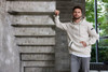 A light beige men's hoodie with a front pocket and a logo, displayed against a modern stone backdrop.