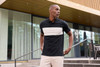A polo shirt featuring a black base with a cream colour-block design, displayed outdoors. It has a logo.