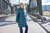 A teal ladies' winter long coat with a hood, featuring a puffer style, worn by a woman on a bridge.