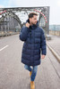 A man walks on a bridge wearing a navy long puffer coat, paired with jeans and tan boots.