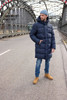 A man wearing a navy puffer coat stands on an empty road, paired with blue jeans and tan boots.