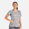 A grey women's V-neck top featuring a playful pattern of colourful cats and other motifs, with visible pockets.