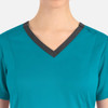 A teal women's top with a contrast dark V-neckline and shoulder accents, featuring a logo on the side.