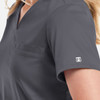 A women's tuckable V-neck top in dark grey, featuring a pocket and a small logo on the sleeve.