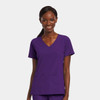 A women’s mock wrap top in purple with a V-neck and two front pockets. The model is smiling while wearing it.