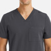 A men's grey V-neck top featuring three pockets and a shoulder snap detail. It has a logo on the left side.