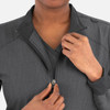 A woman adjusts the zipper of a grey, high-collar warm-up jacket with a logo.