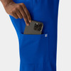 A close-up of a hand placing a phone into the pocket of bright blue women's skinny pull-on pants, featuring a logo.