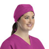 A unisex scrub cap in bright pink, featuring buttons, worn by a woman with a ponytail and a scrubs outfit.