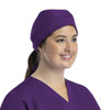 A unisex scrub cap in purple with buttons, worn by a smiling individual in scrubs.