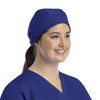 A unisex scrub cap in navy blue with buttons, worn by a smiling model.