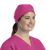 A pink unisex scrub cap with buttons displayed on a model, featuring a tied back design.