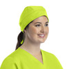 A unisex scrub cap in bright yellow with buttons, worn by a smiling woman with a ponytail.