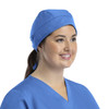 A unisex scrub cap in blue with buttons, worn by a smiling individual in scrubs.