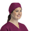 A unisex scrub cap in a rich burgundy colour with buttons, worn by a smiling woman.