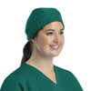 A green unisex scrub cap with buttons, worn by a smiling woman in a medical uniform.